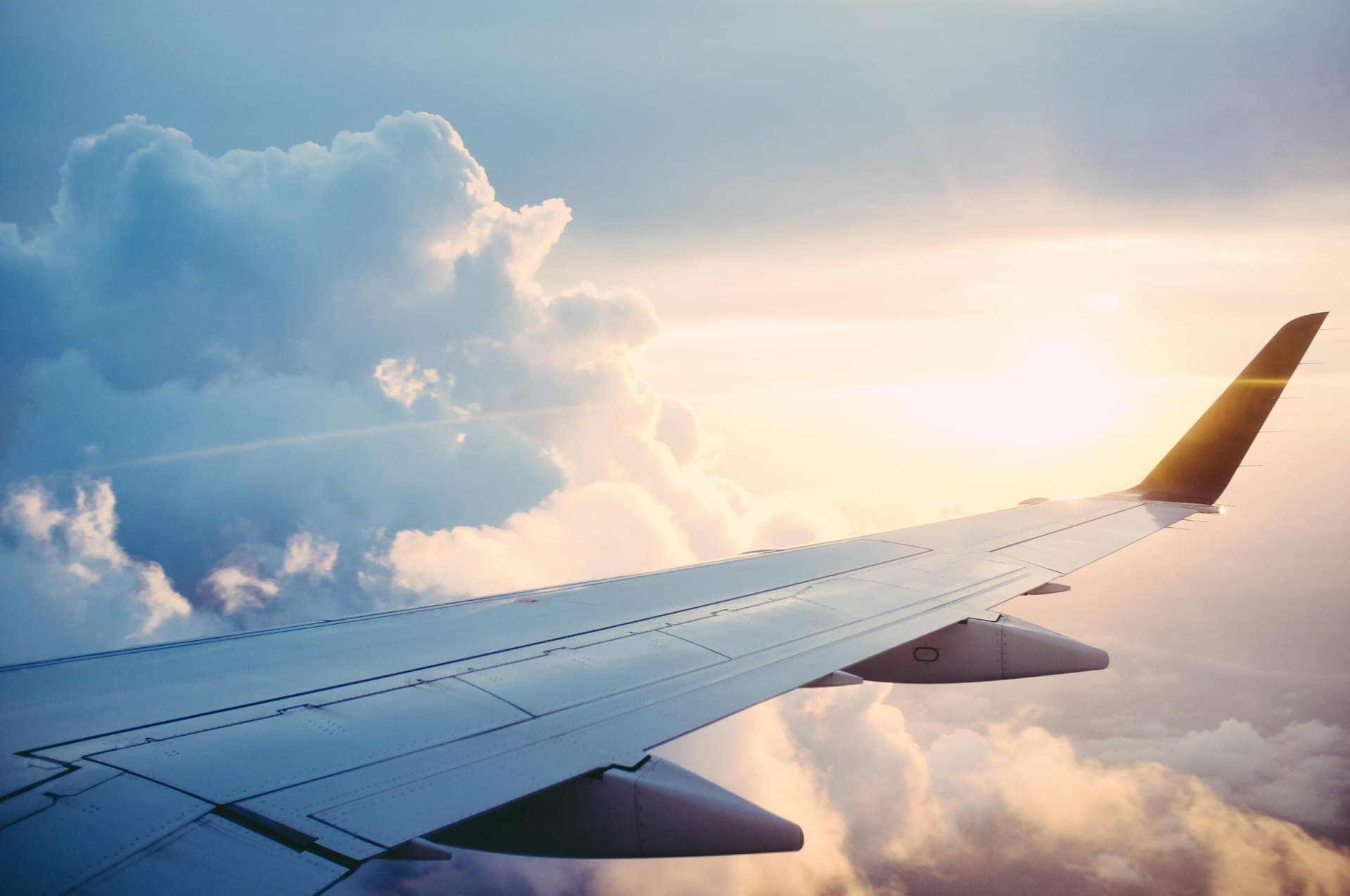 An airplane wing above the clouds, lit by a golden sunrise.