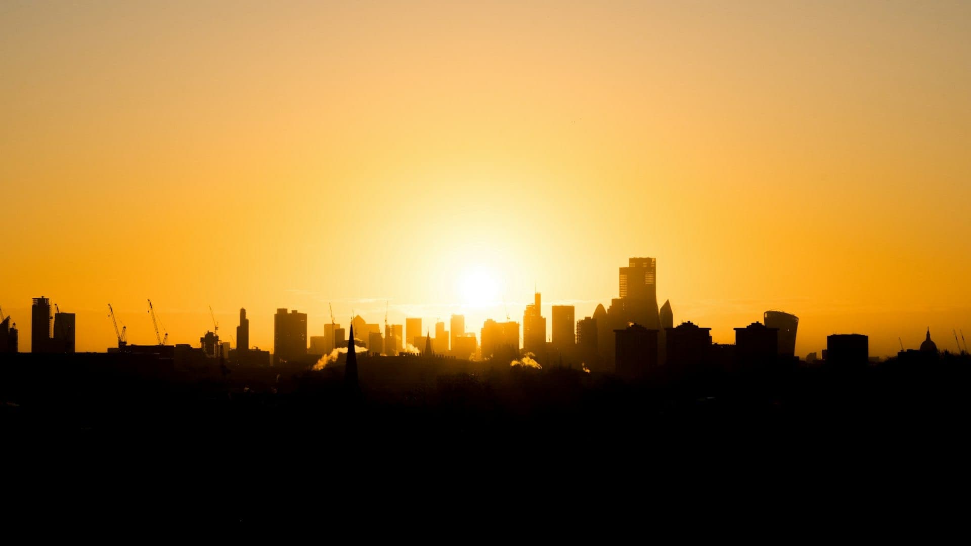 A city skyline silhouetted against a warm golden sunrise.